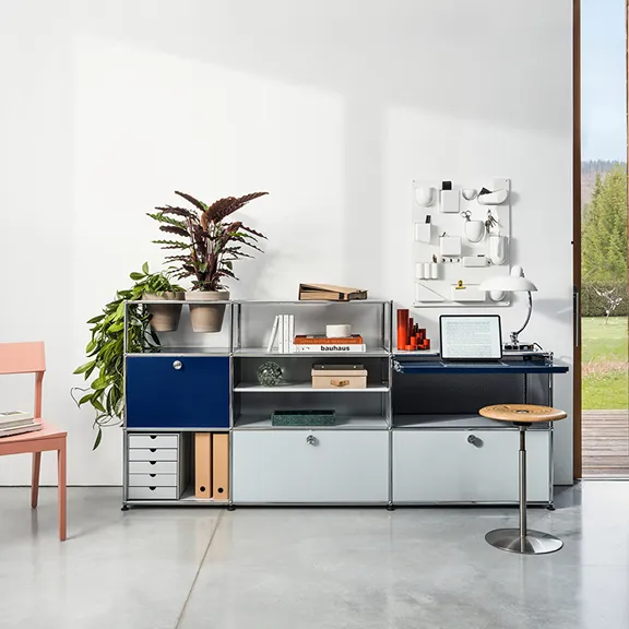 Blau-graues USM Chrom-Regalsystem mit integriertem Arbeitsplatz, Laptop und Zimmerpflanzen in einem hellen Raum.