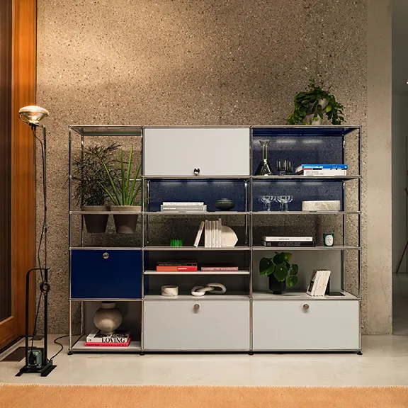 Großes USM Chrom-Regalsystem mit grauen und blauen Elementen vor einer Steinwand, dekoriert mit Pflanzen und Büchern.